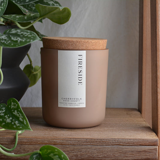 a scented candle in a matte sand colored glass jar labeled with fireside