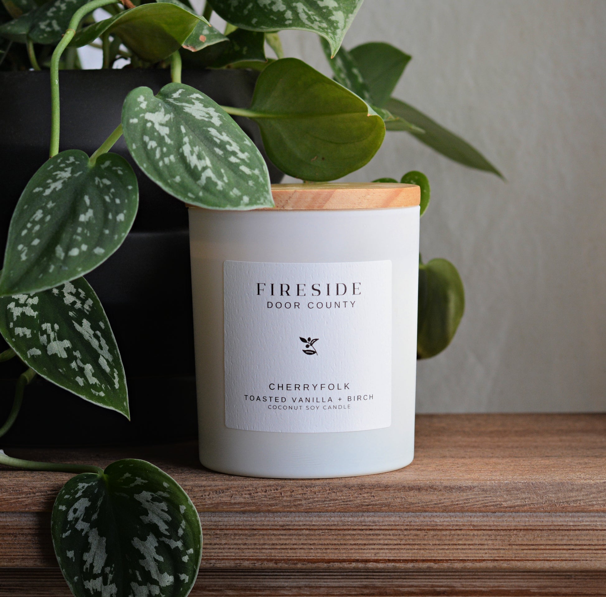 A white scented candle labeled fireside door county with bamboo lid